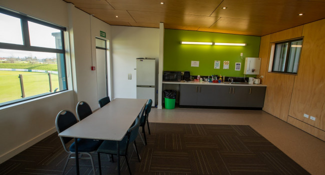 Oval VOC meeting room with table and 6 chairs. Small kitchenette in background