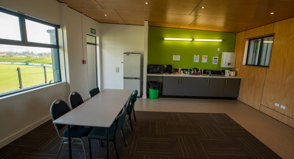 Oval VOC meeting room with table and 6 chairs. Small kitchenette in background
